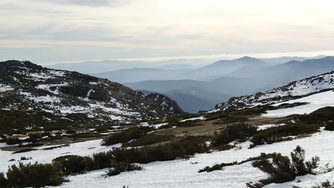 Snodekt høyfjell i Serra da Estrela med lyng mellom snoflekkene og blå åsrygger i disen bak