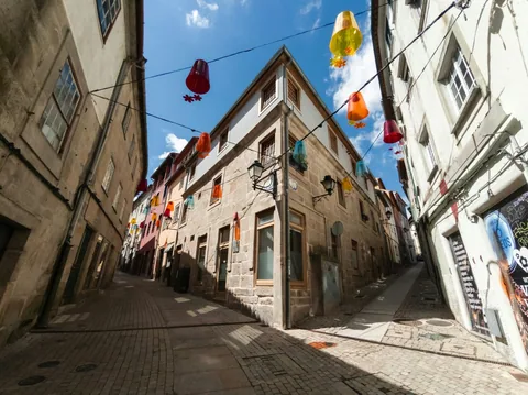 Smal brosteinsgate i gamlebyen i Viseu med fargerike papirlykter hengende mellom gamle steinhus