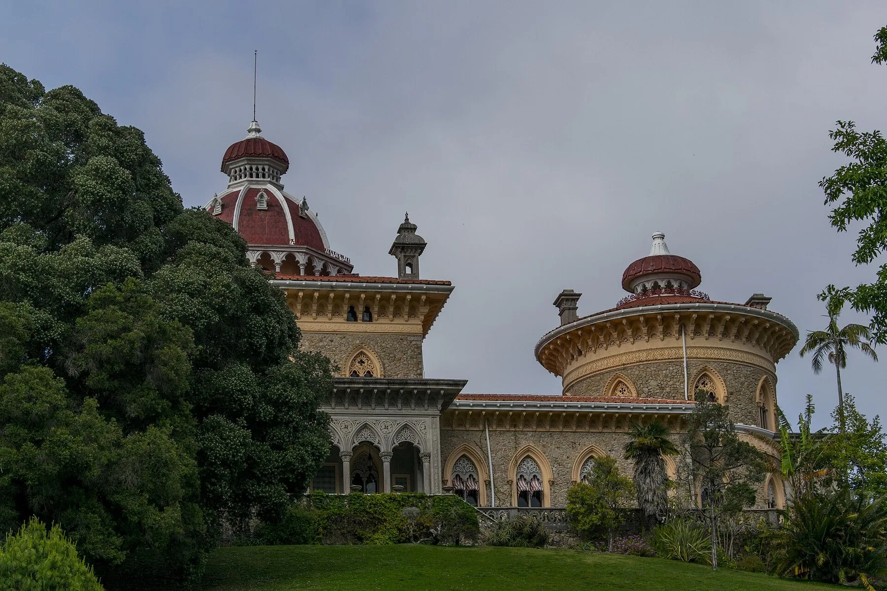 Palácio de Monserrate med røde kupler og mauriske detaljer bak store trær og en grønn plen i Sintra
