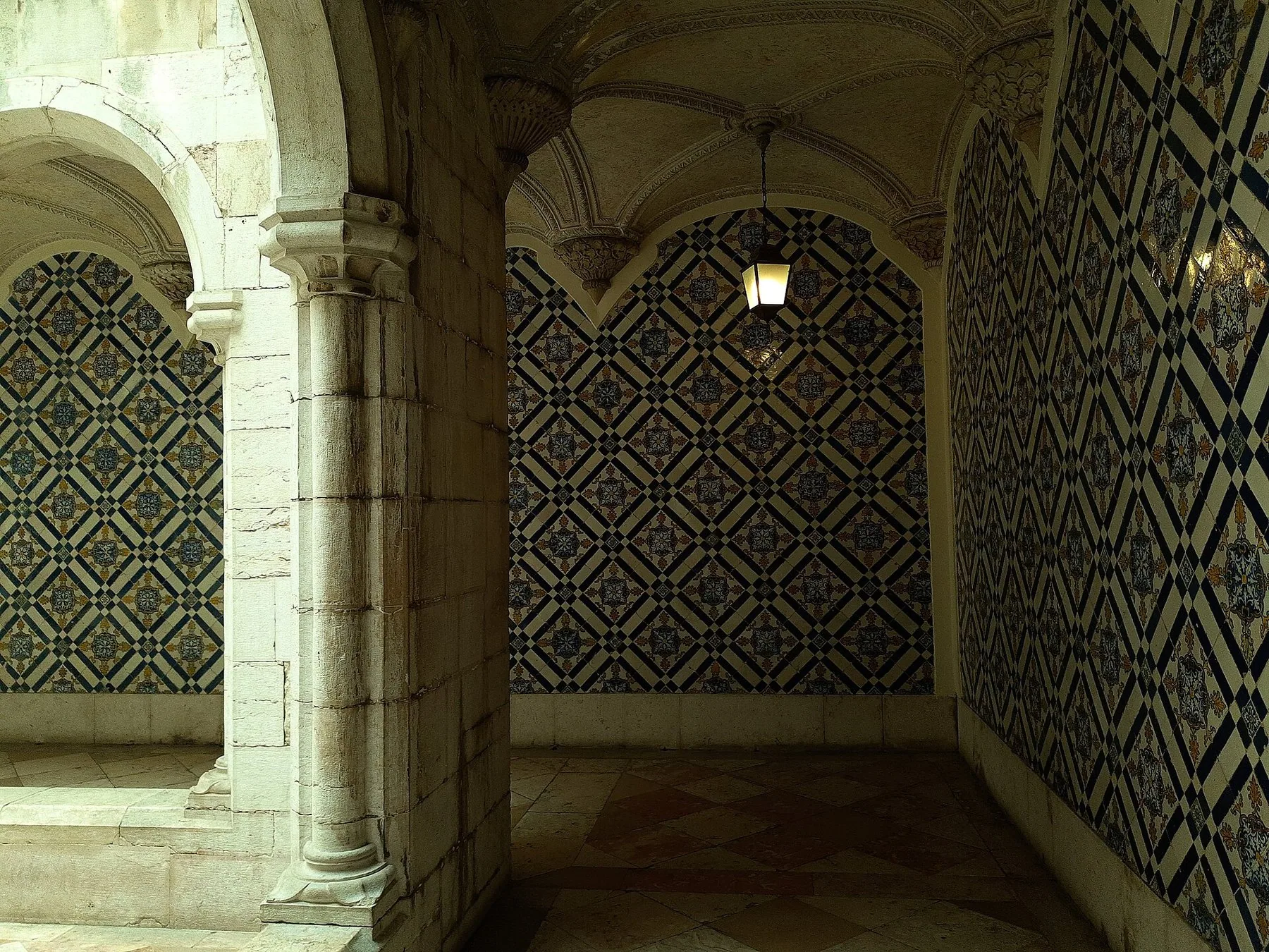 Klostergang med steinbuer og vegger dekket av mønstrede blå og gule azulejos i Museu Nacional do Azulejo