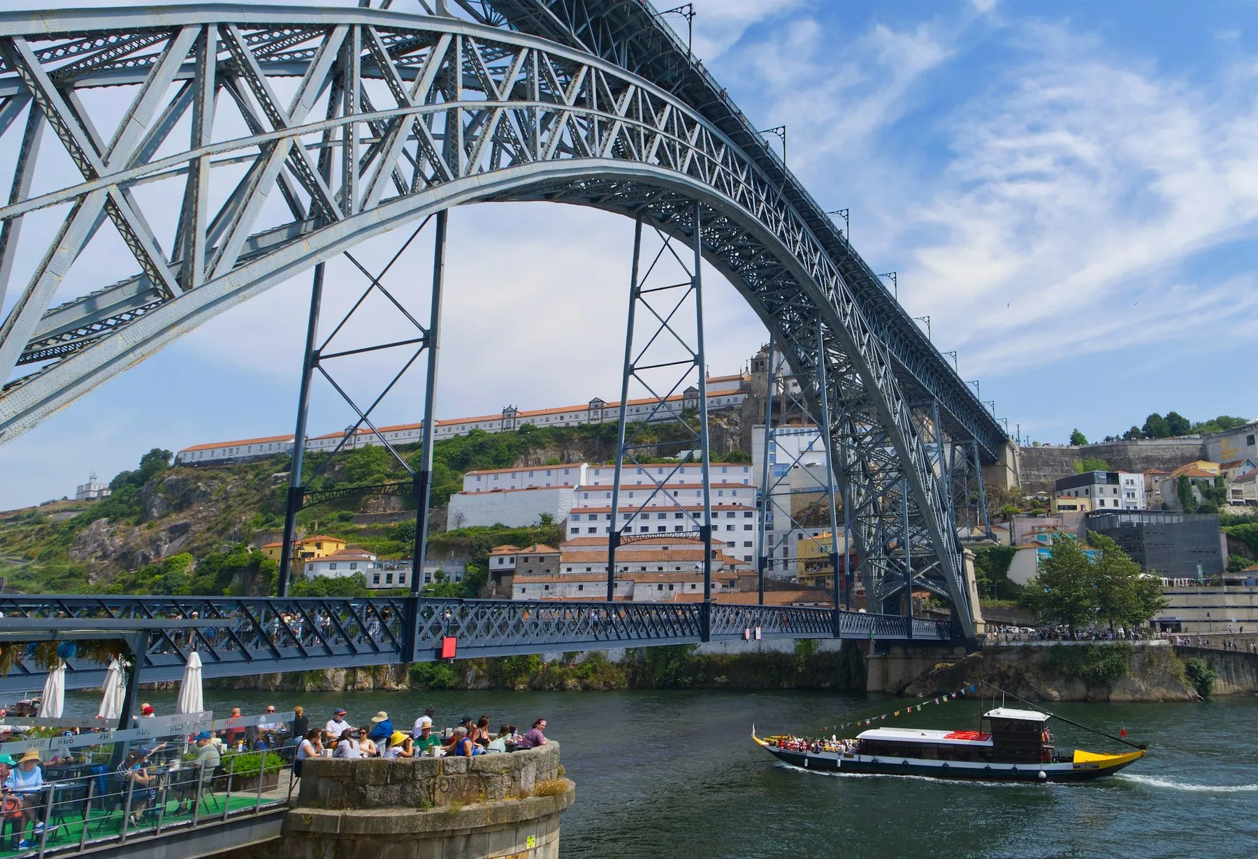 Jernbuen på Ponte Dom Luís I over Douro, med en rabelo-båt på elva og Serra do Pilar bak broen