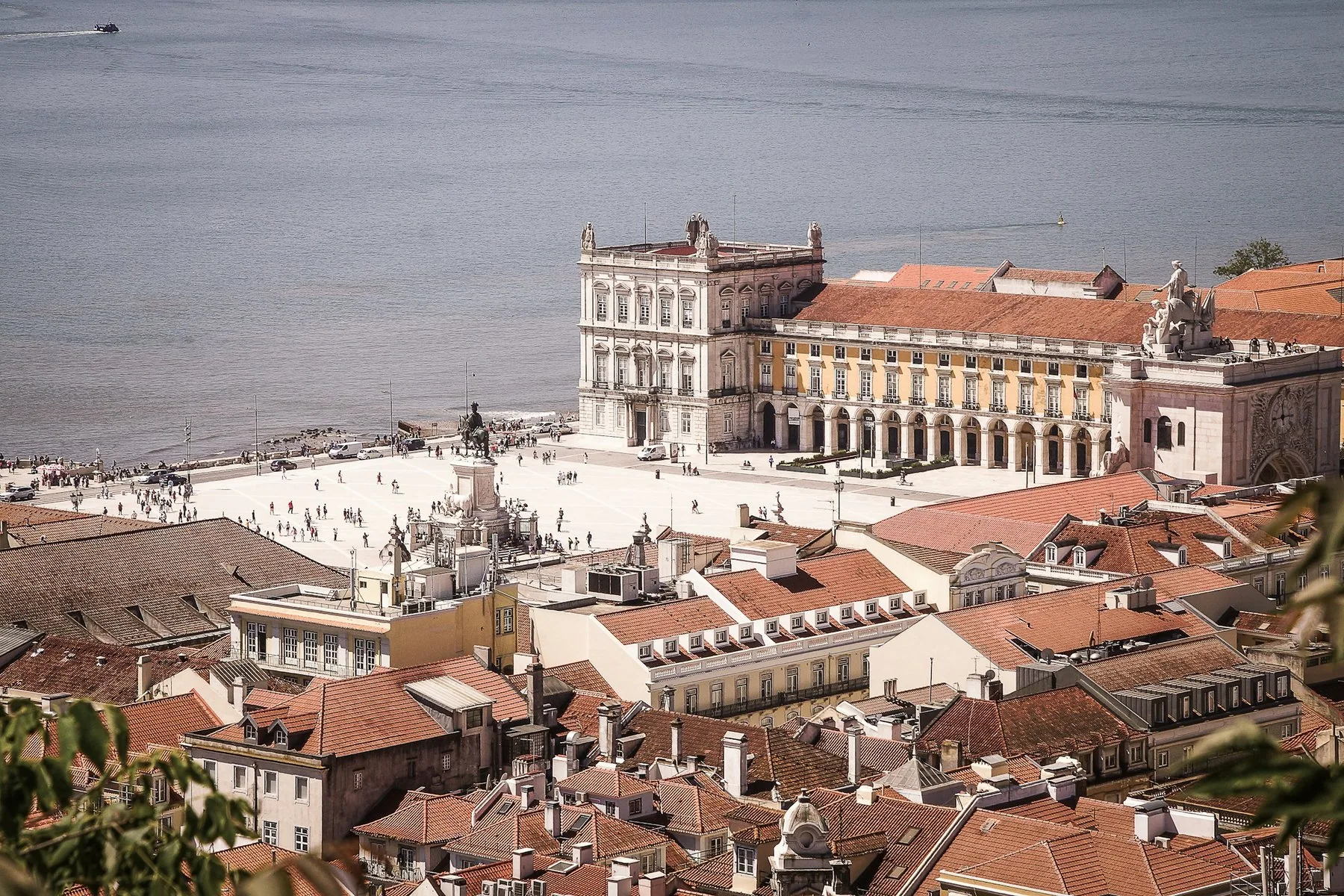Praça do Comércio sett ovenfra over røde hustak i Baixa, med gule arkader og Tejo bak plassen