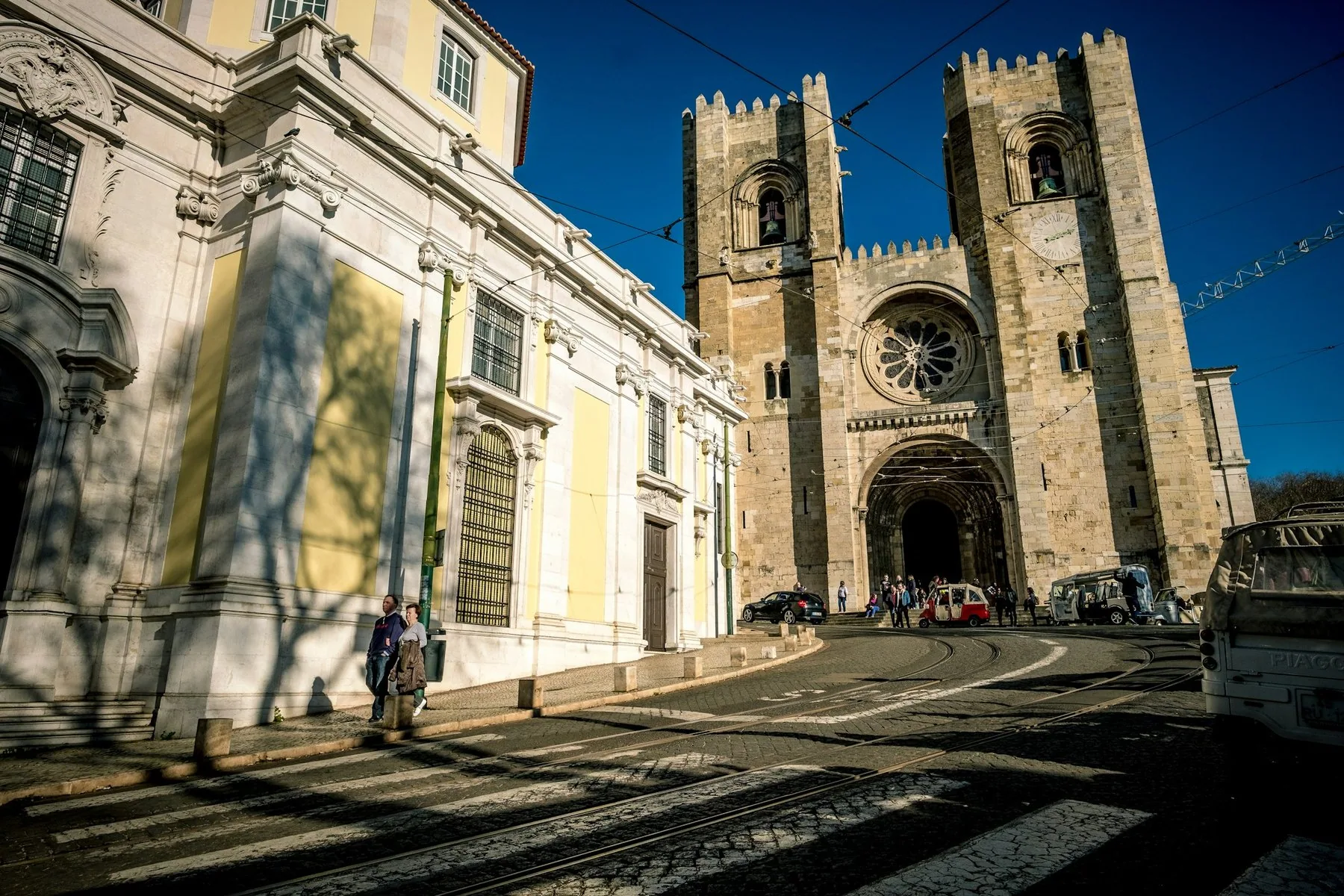 Den romanske fasaden på Sé-katedralen i Lisboa med to tårn og rosevindu, sett fra gata i skarpt sollys
