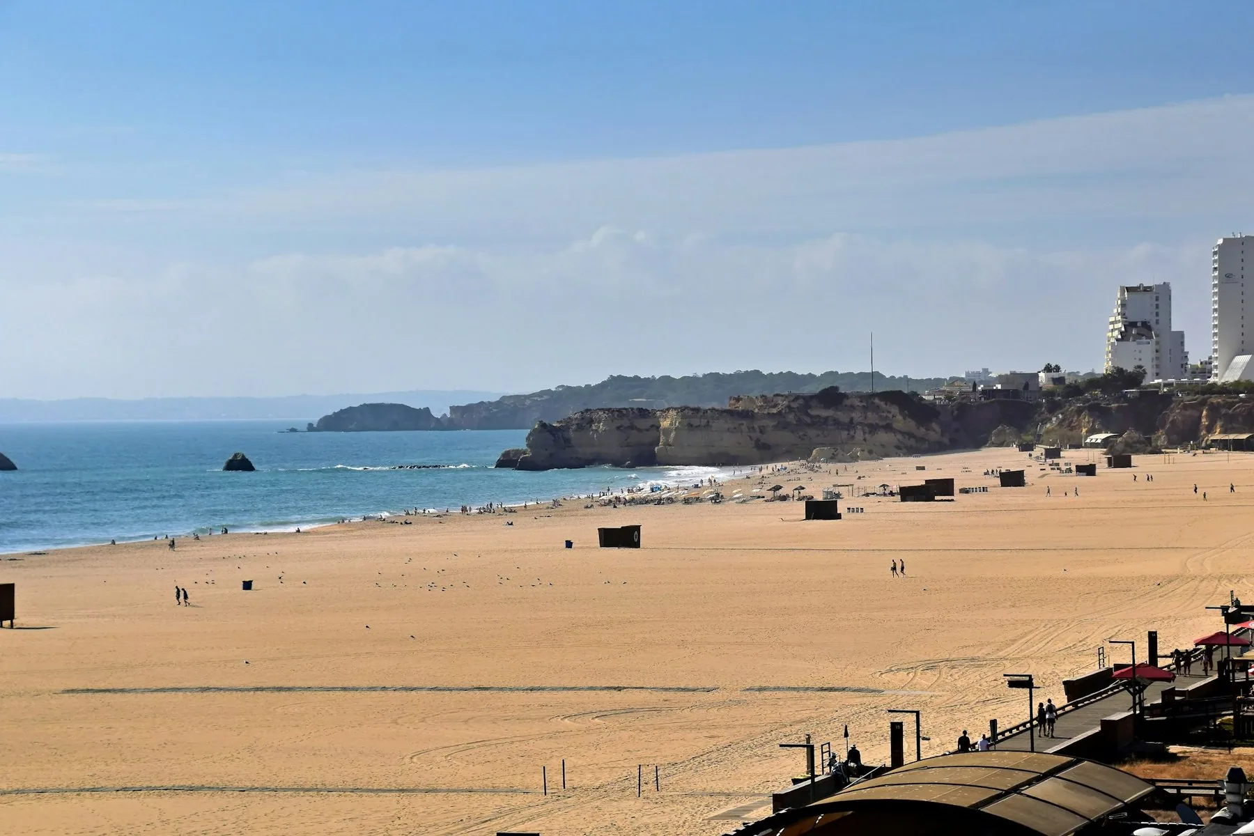 Bred sandstrand med rolige bølger og hvite hus i det fjerne i Algarve