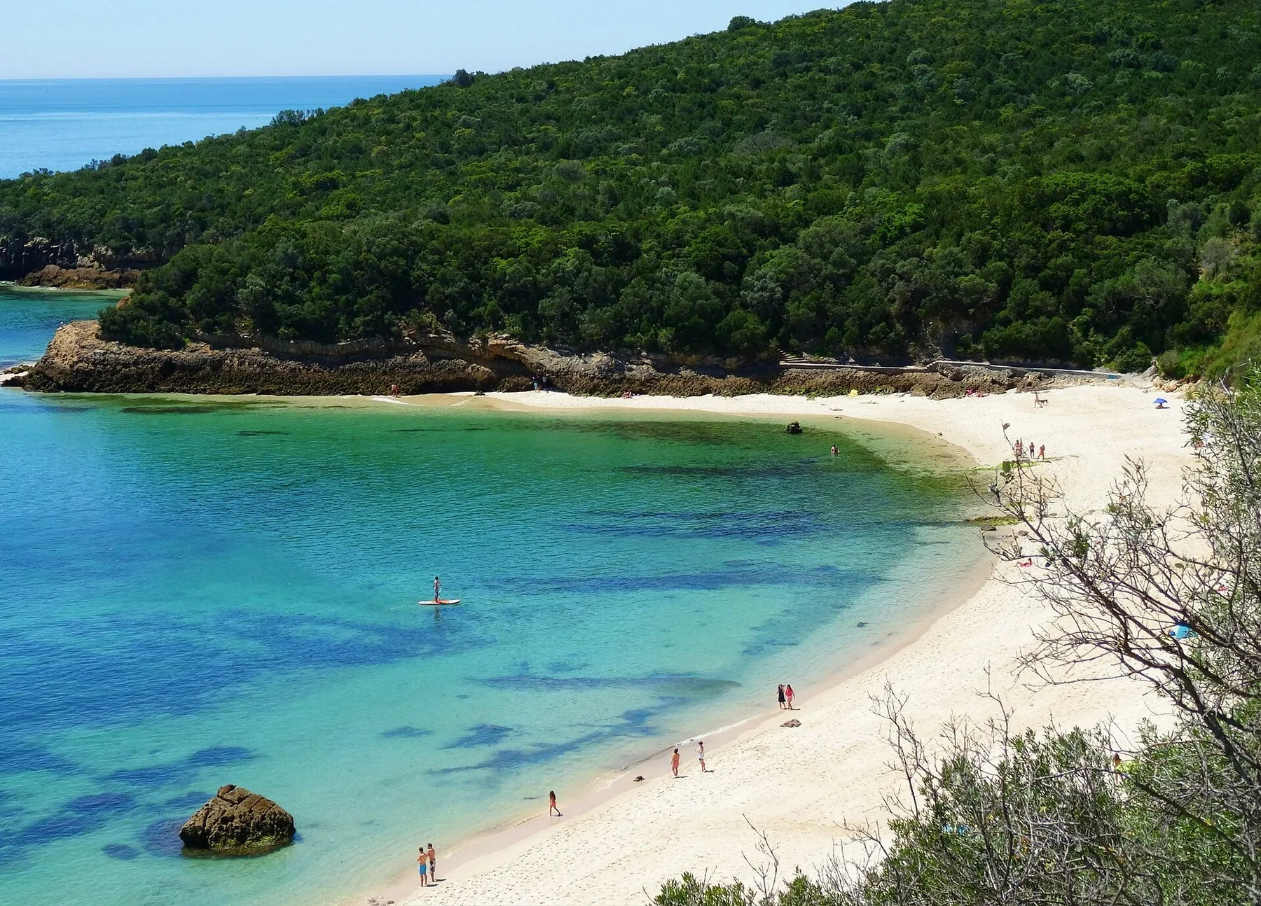 Turkis bukt med lys sandstrand ved Galapos under de skogkledde åsene i Serra da Arrábida