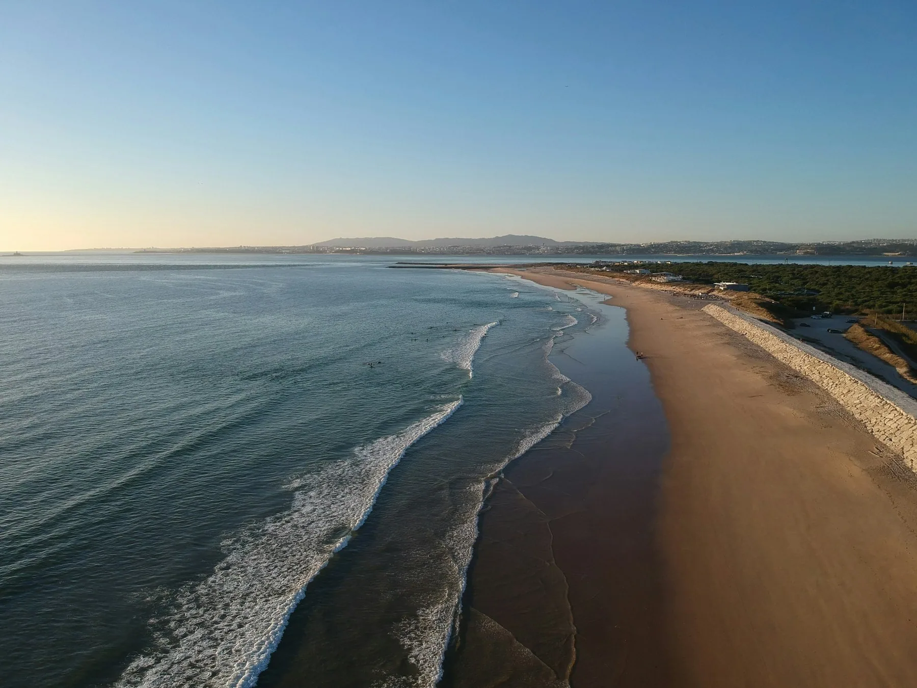 Luftfoto av den lange sandstranden og bølgene ved Costa da Caparica sør for Lisboa