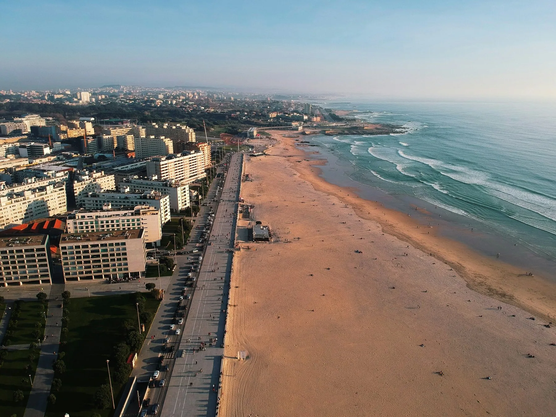 Flyfoto av den lange sandstranden i Matosinhos med bølger, strandpromenade og boligblokker i kveldslys