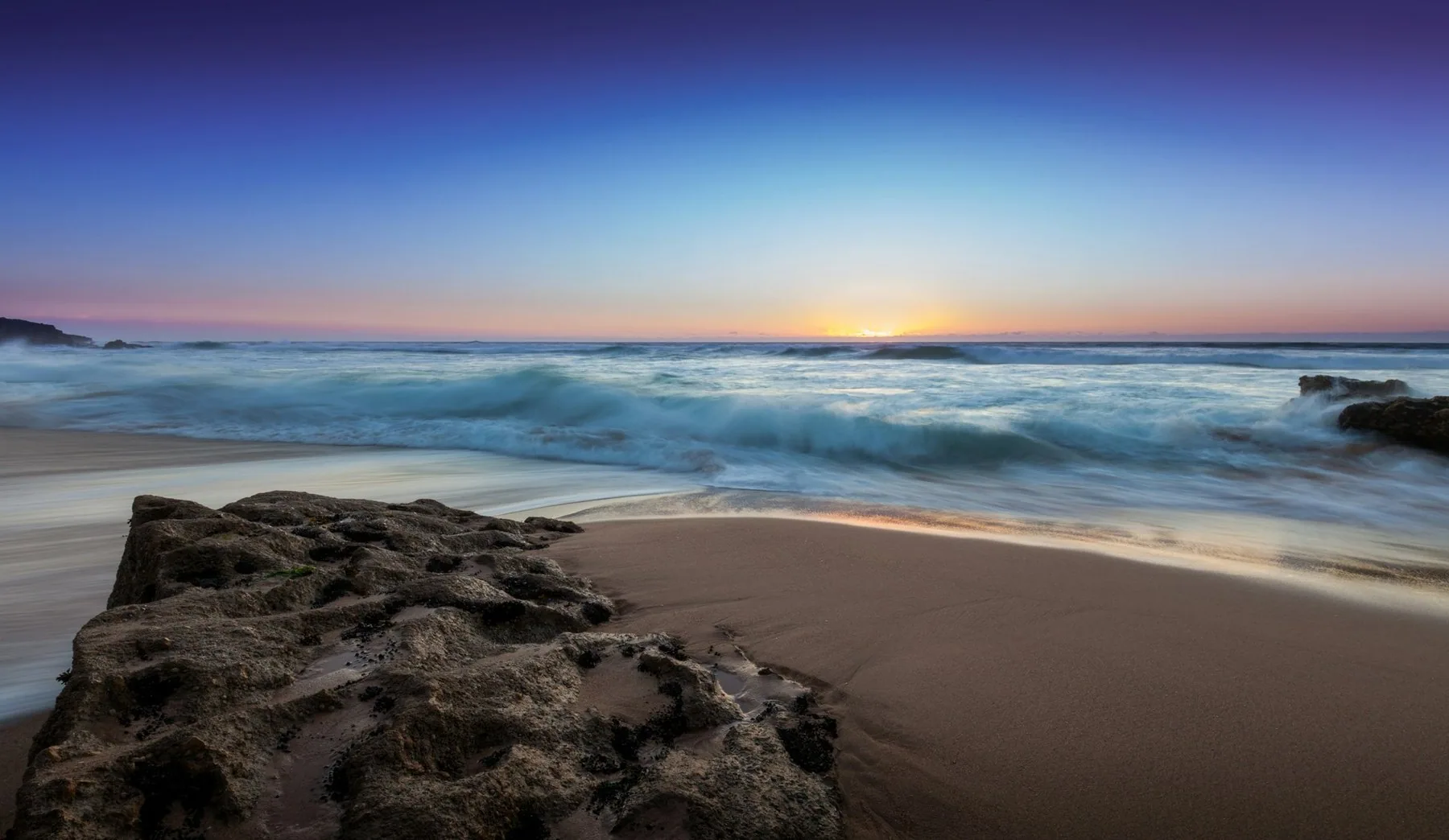 Praia do Guincho ved Cascais i kveldssol, med våt sand og klipper mot Atlanterhavet