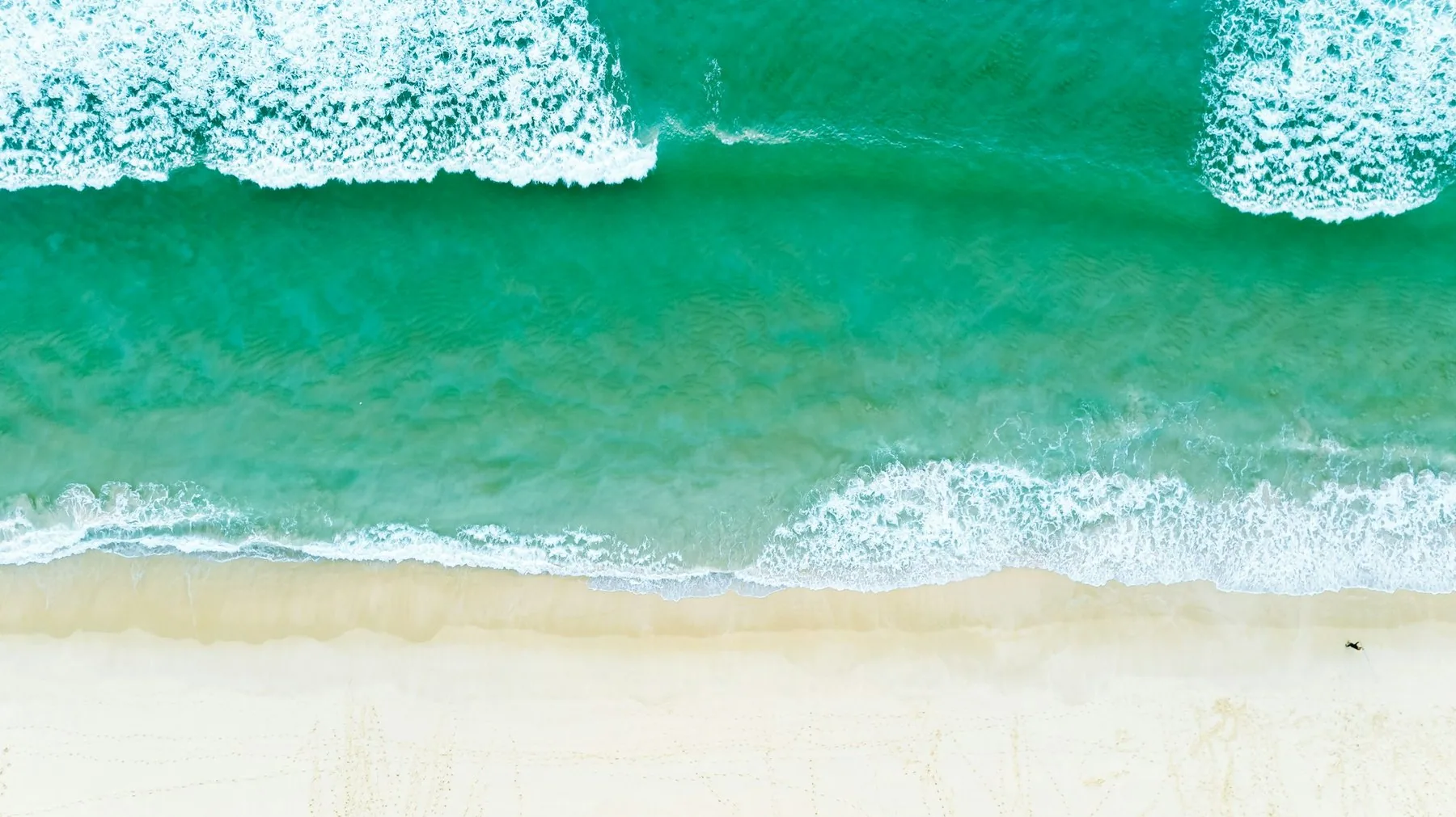 Praia da Comporta sett ovenfra, med lys sand og turkise bølger som ruller inn fra Atlanterhavet