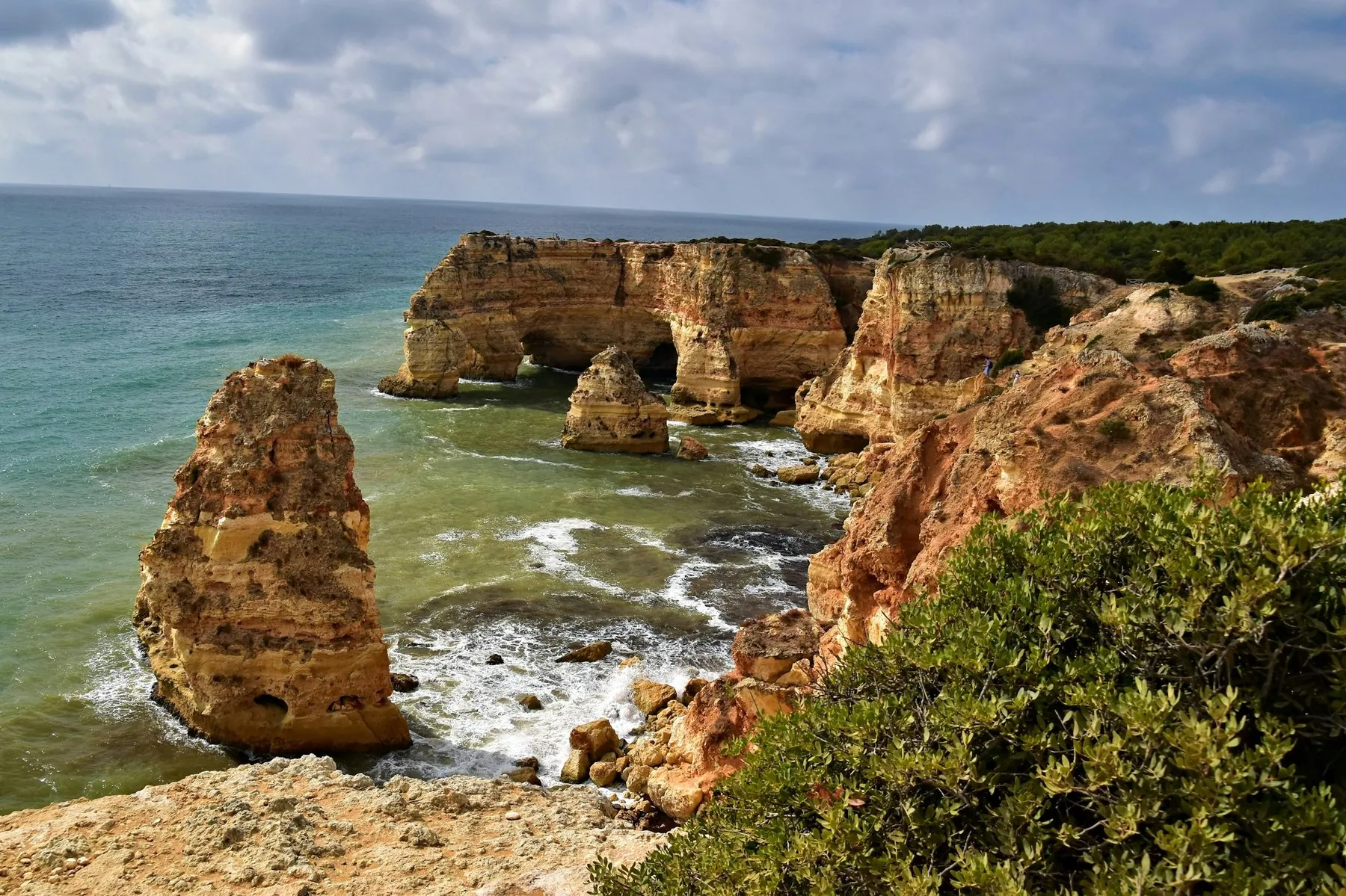 Drivende skyer over sandsteinsklipper og klippesøyler ved Praia da Marinha, der bølgene slår inn mot fjellet