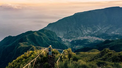 Turgåer ved rekkverket på en fjellkant på Madeira, med grønne daler og en landsby langt under